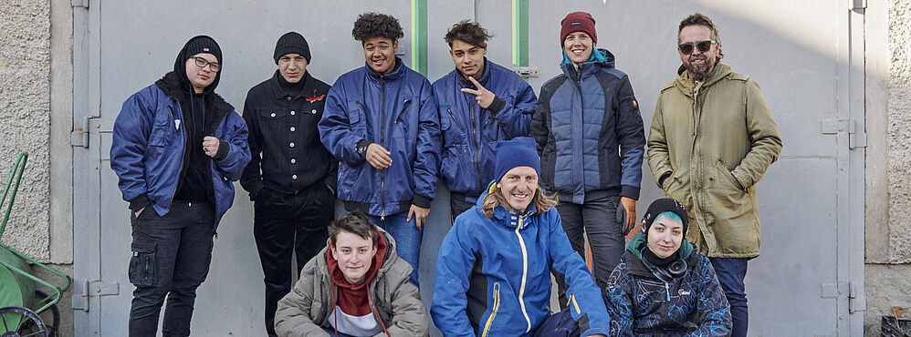 Eine Gruppe an Jugendlichen und Trainer_innen posiert für ein Foto vor der Werkstatt