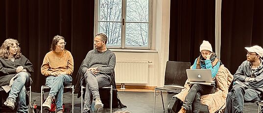 Netzwerktreffen – Menschen sitzen im Kreis auf Stühlen, unterhalten sich und machen sich Notizen auf ihren Laptops.