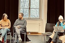 Netzwerktreffen – Menschen sitzen im Kreis auf Stühlen, unterhalten sich und machen sich Notizen auf ihren Laptops.