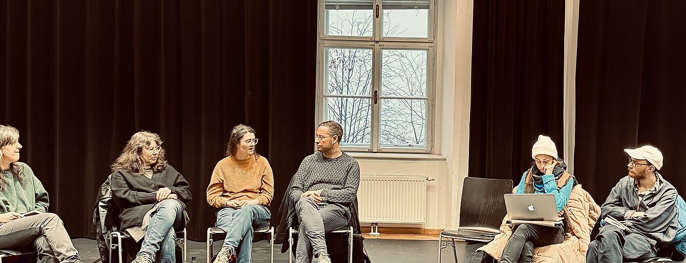 Netzwerktreffen – Menschen sitzen im Kreis auf Stühlen, unterhalten sich und machen sich Notizen auf ihren Laptops.