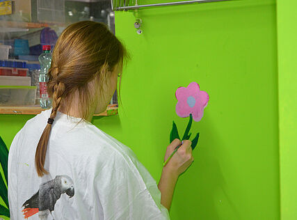 Eine junge Frau malt eine Blume an eine Wand