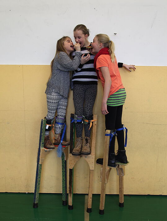 Drei Mädchen auf Stelzen vor einer Wand