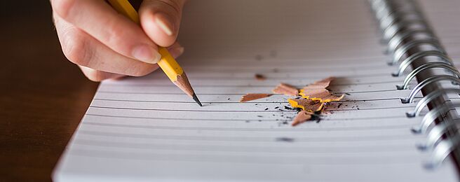 eine Hand mit Bleistift schreibt in einen Notizblock