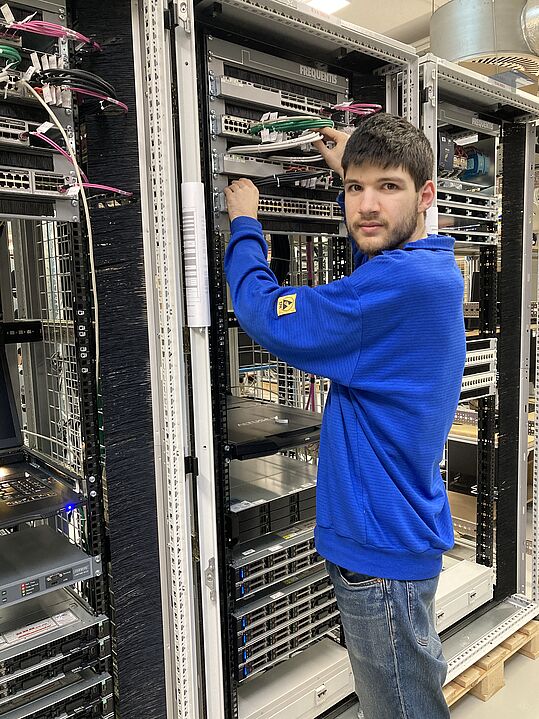 Person in blauem Pullover arbeitet an einem Serverrack mit Netzwerkkabeln in einem Rechenzentrum.