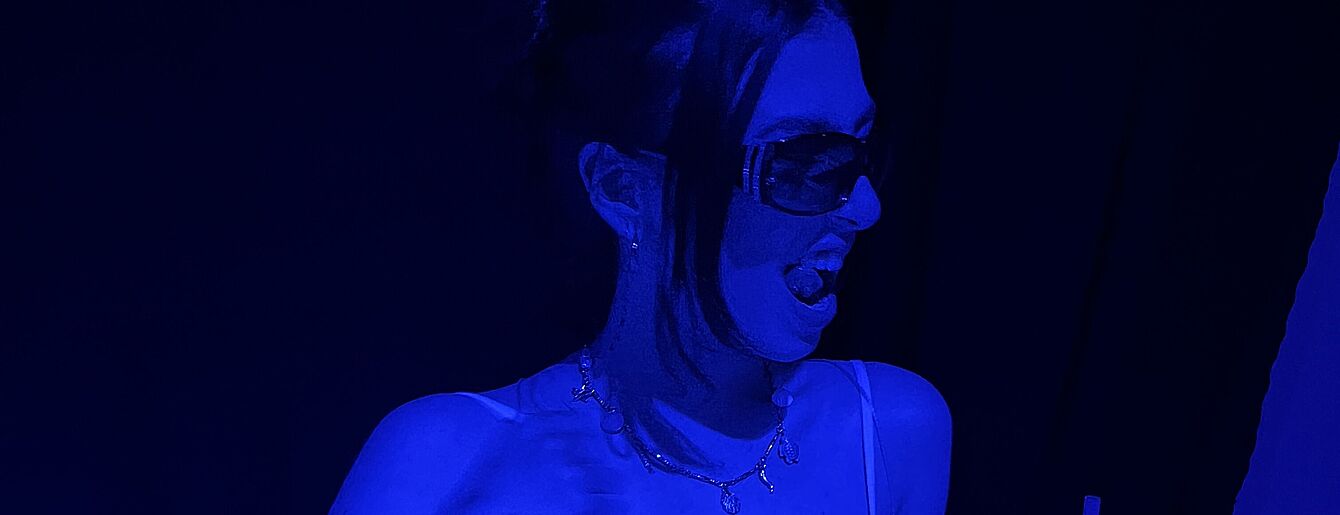 Vicky mit Sonnenbrille und Halskette bei Event, blau beleuchtet