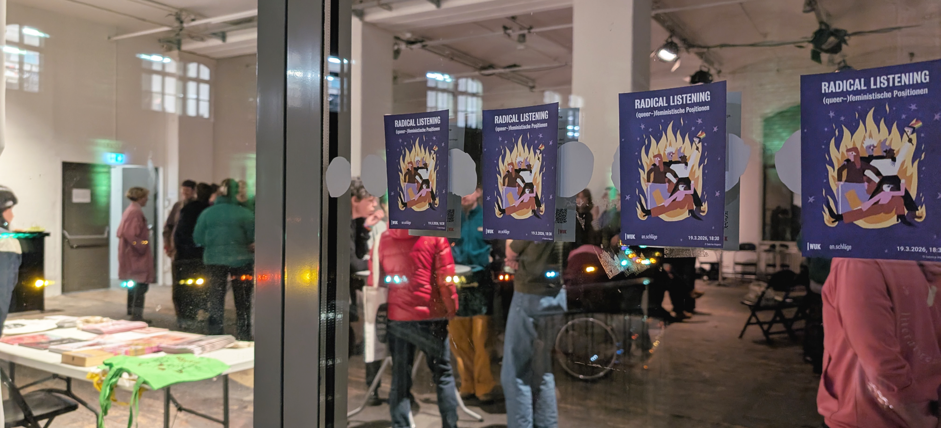 Mehrere Plakate mit der Aufschrift 'RADICAL LISTENING (queer-feministische Positionen)' kleben an einer Glaswand, dahinter stehen Menschen in einem Veranstaltungsraum mit Tischen und Stühlen