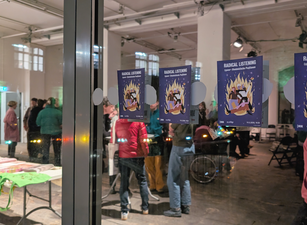 Mehrere Plakate mit der Aufschrift 'RADICAL LISTENING (queer-feministische Positionen)' kleben an einer Glaswand, dahinter stehen Menschen in einem Veranstaltungsraum mit Tischen und Stühlen