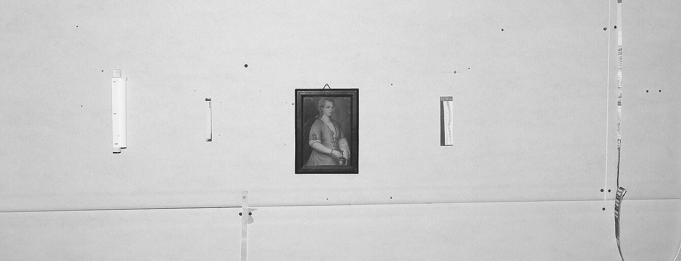 Wand mit Resten von ehemals aufgehängten Artefakten sowie einem kleinen gemalten und gerahmte Bild einer Frau