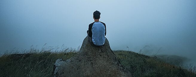 Ein Mensch sitzt alleine in einer nebeligen Landschaft