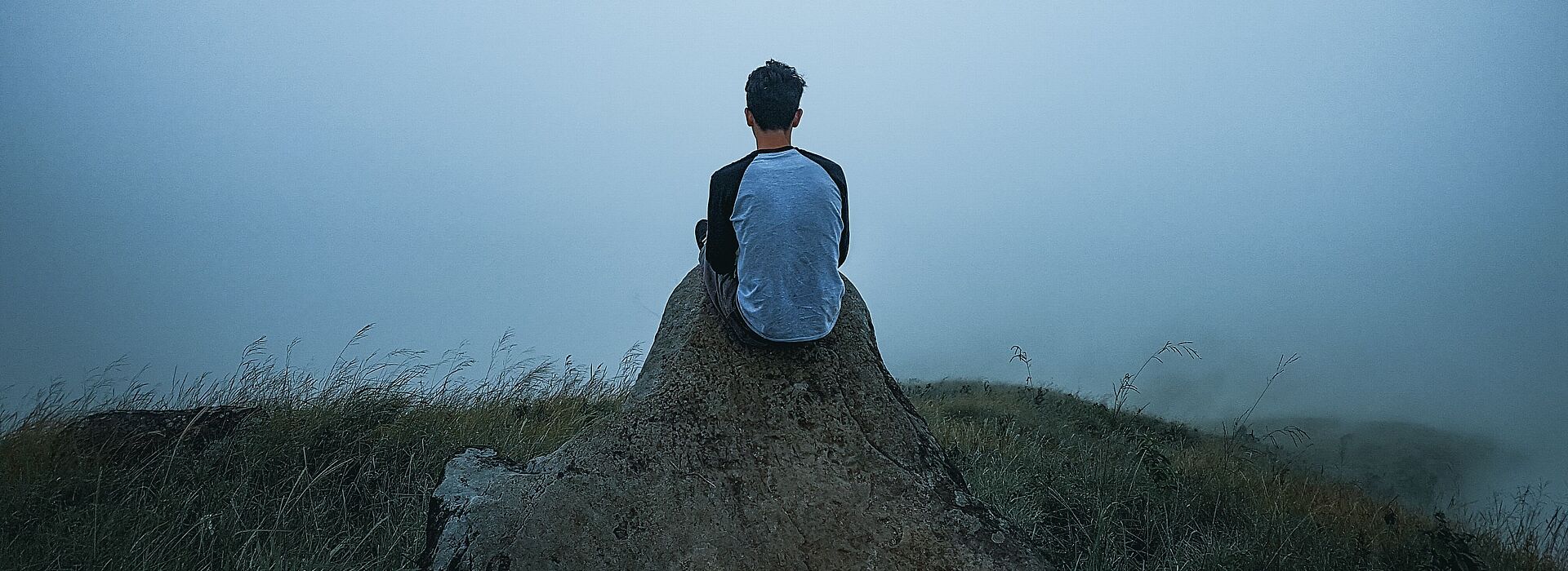 Ein Mensch sitzt alleine in einer nebeligen Landschaft