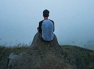 Ein Mensch sitzt alleine in einer nebeligen Landschaft