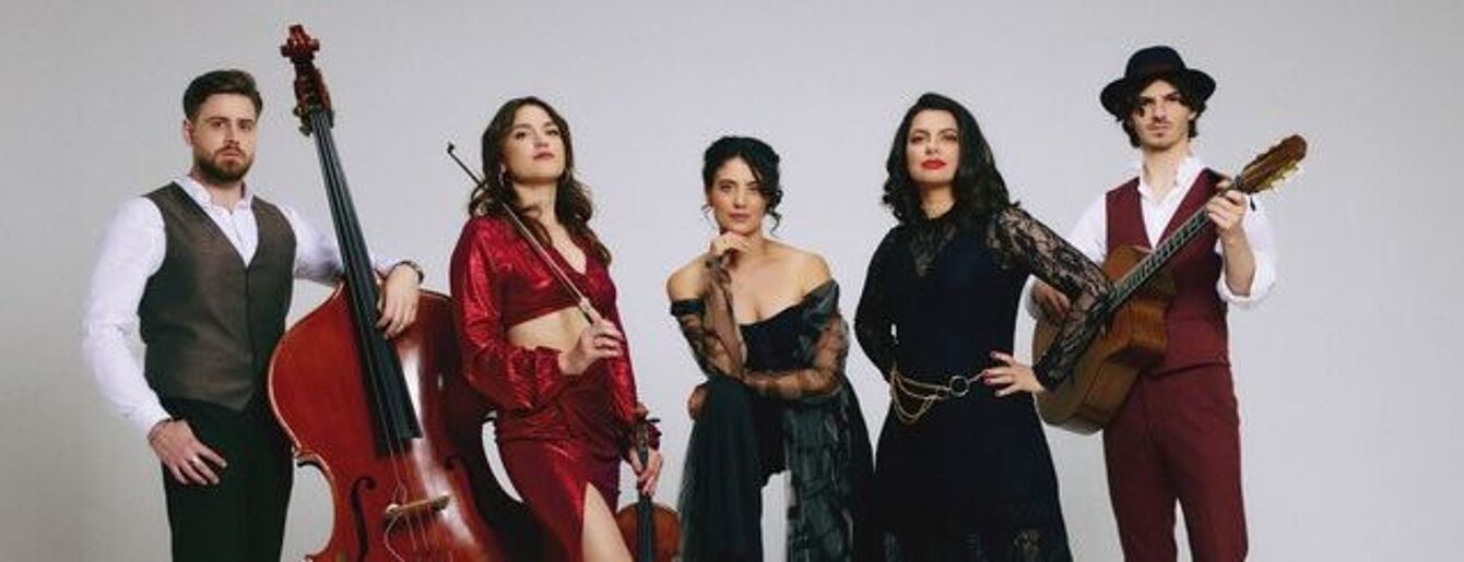 Fünf Personen in eleganter Kleidung posieren vor neutralem Hintergrund, eine spielt Kontrabass, eine hält eine Geige, eine trägt einen Hut und eine Gitarre