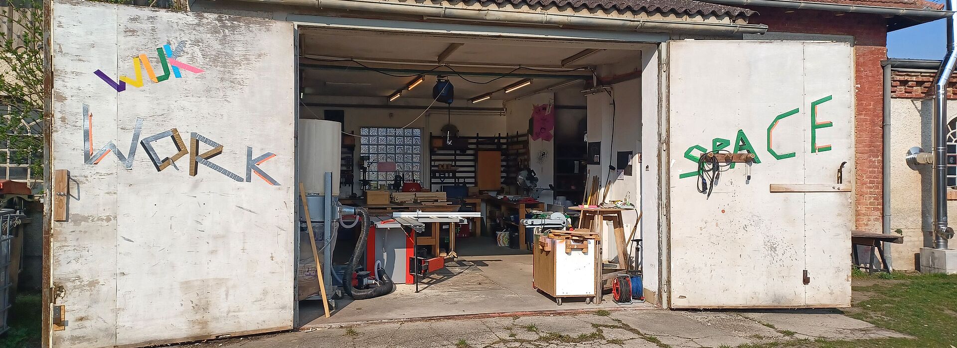 Offene Werkstatttore an einem Gebäude mit sichtbaren Werkzeugen und Werkbänken im Inneren