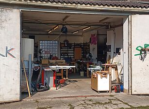 Offene Werkstatttore an einem Gebäude mit sichtbaren Werkzeugen und Werkbänken im Inneren