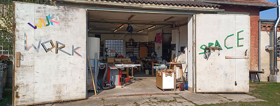 Offene Werkstatttore an einem Gebäude mit sichtbaren Werkzeugen und Werkbänken im Inneren