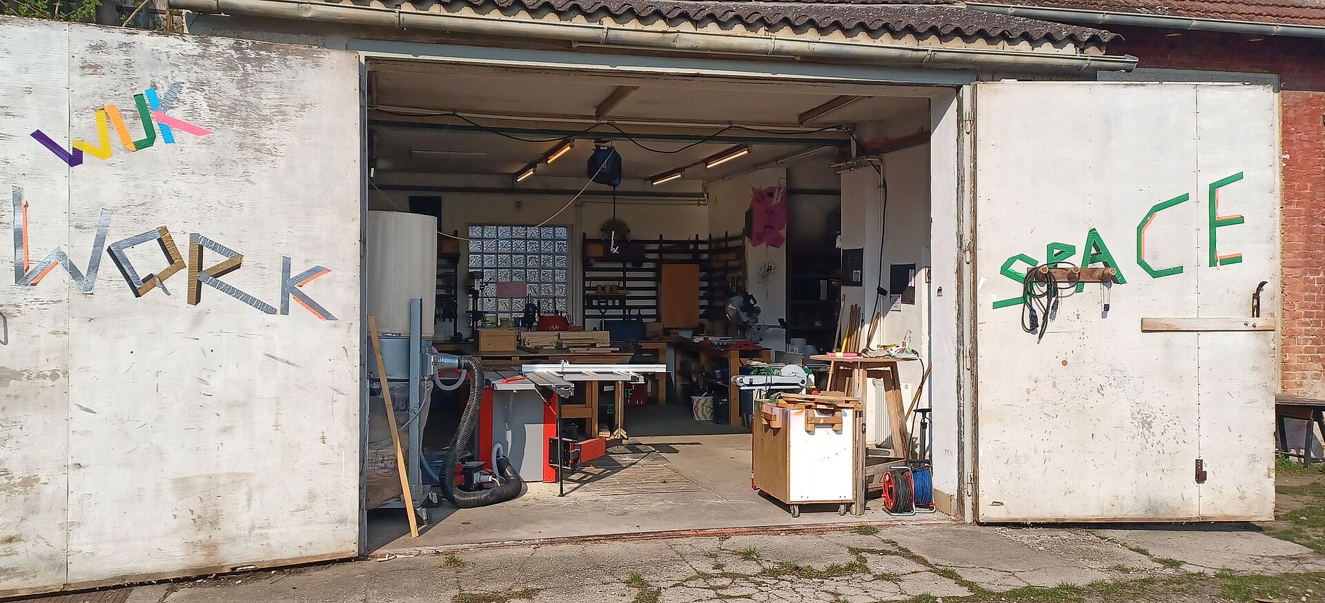 Offene Werkstatttore an einem Gebäude mit sichtbaren Werkzeugen und Werkbänken im Inneren