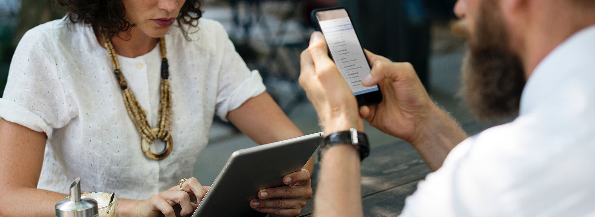 Frau mit Tablet und Mann mit Mobiltelefon sitzen sich gegenüber