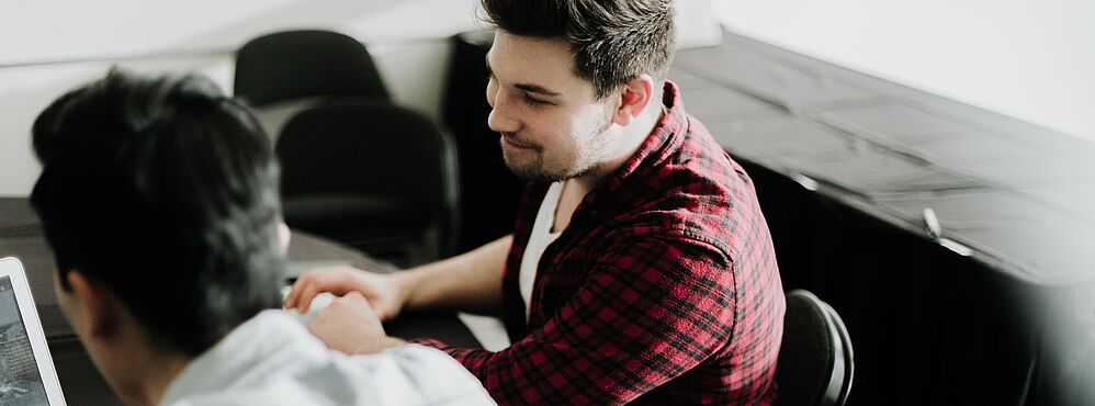 Photo by Priscilla Du Preez on Unsplash Zwei Personen sitzen an einem Tisch, einer zeigt dem anderen etwas auf einem Laptop, Bildungsberatung bei A|B|O Jugend