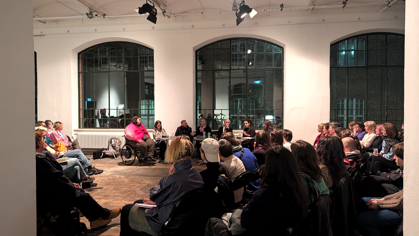 Menschen sitzen in einem großen Raum in einem Stuhlkreis und hören einer Person zu