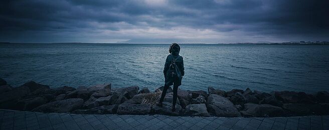 Person von hinten vor Meer und bewölktem Himmel