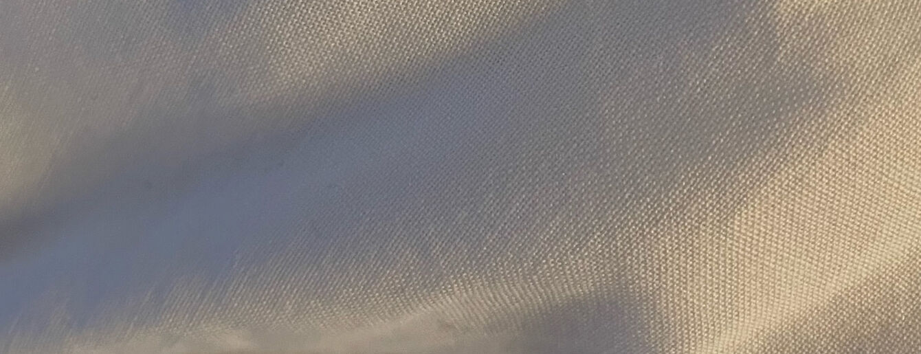 A photograph of warm light over a soft beige linen blanket. Waves of shades and a play of light and depth over its landscape.
