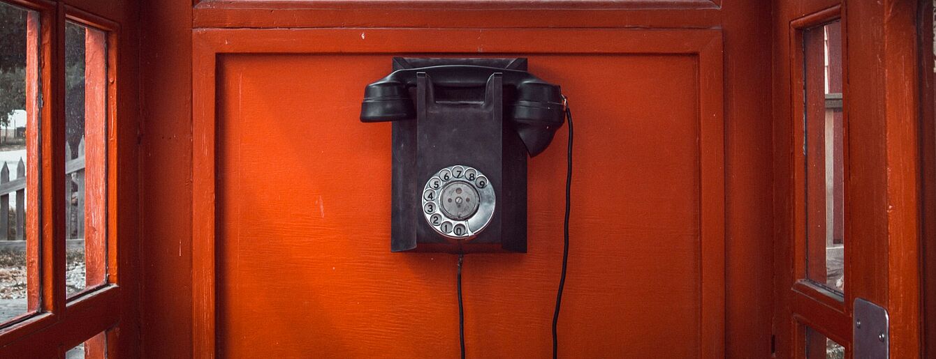 Foto von Antoine Barrès auf Unsplash schwarzes Wählscheibentelefon an roter Holzwand in Telefonzelle