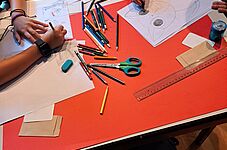 Kinder zeichnen an einem Tisch mit verstreuten Buntstiften, Schere, Linealen und Radiergummi