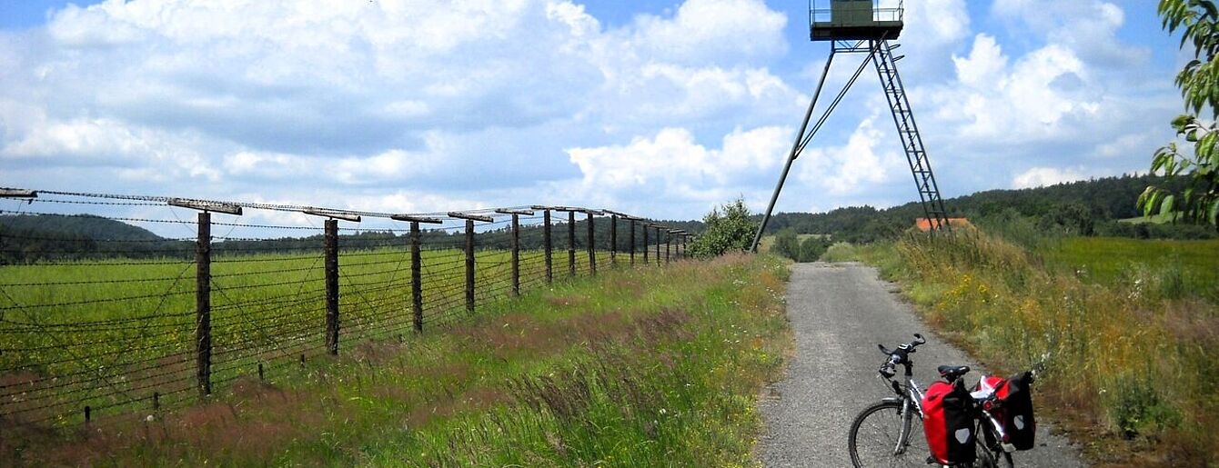 Ein weg bis zum Horizont entlang einem Zaun. Auf dem Weg steht ein bepacktes Fahrrad.