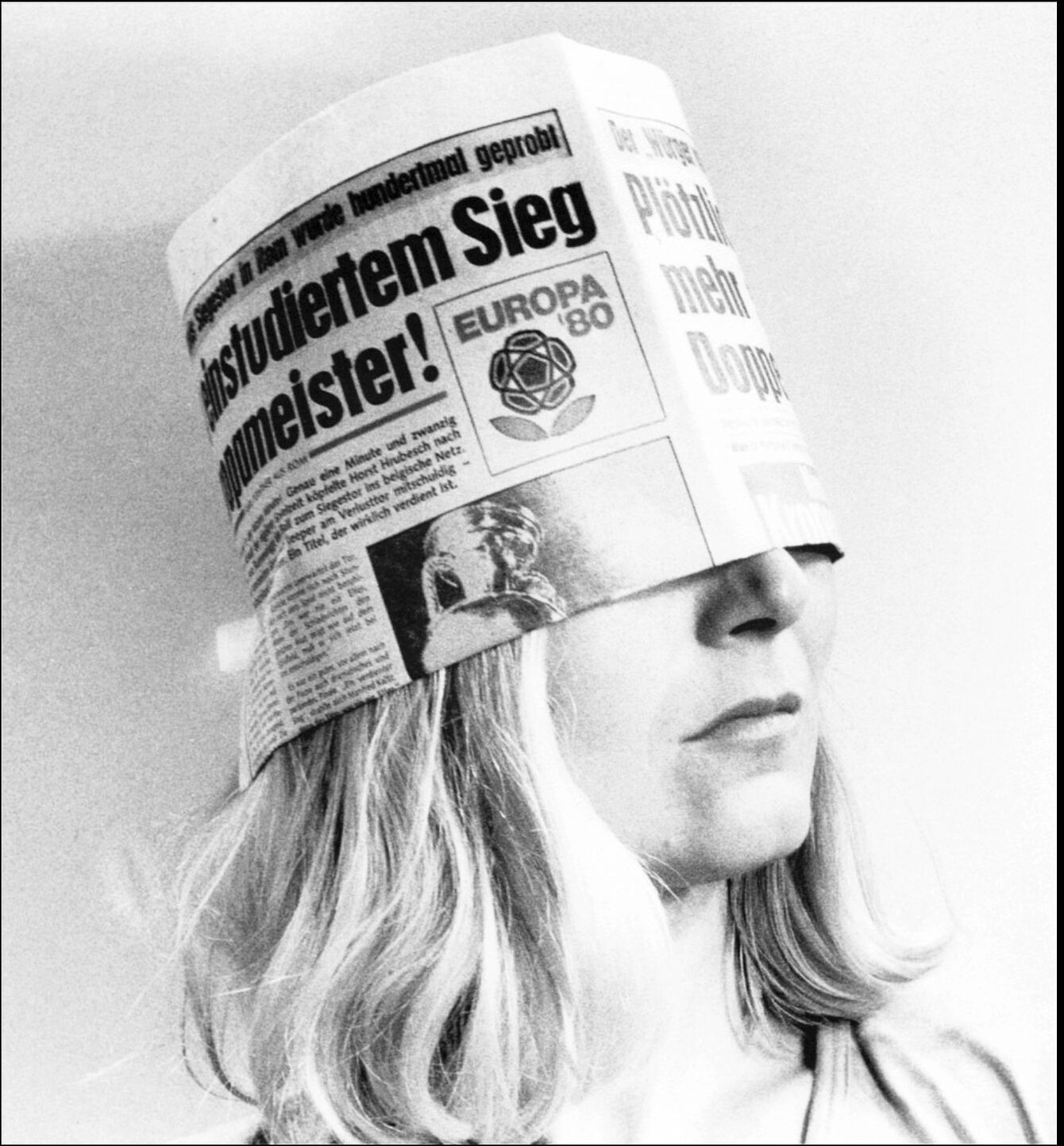 Person mit langem Haar trägt eine Kopfbedeckung aus einer Zeitung