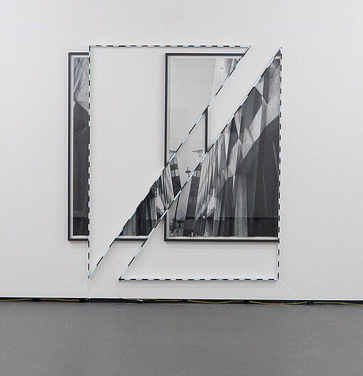 Zwei schwarz-weiße gerahmte Fotografien an einer weißen Wand, teilweise von einem diagonalen Spiegelstück überlagert