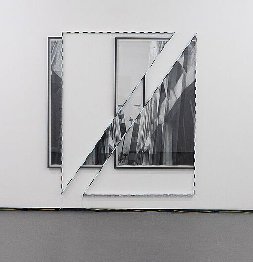 Zwei schwarz-weiße gerahmte Fotografien an einer weißen Wand, teilweise von einem diagonalen Spiegelstück überlagert
