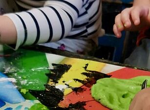 Kinderhände formen grüne Knetmasse auf einem bunt bemalten Tisch mit Regenbogenfarben