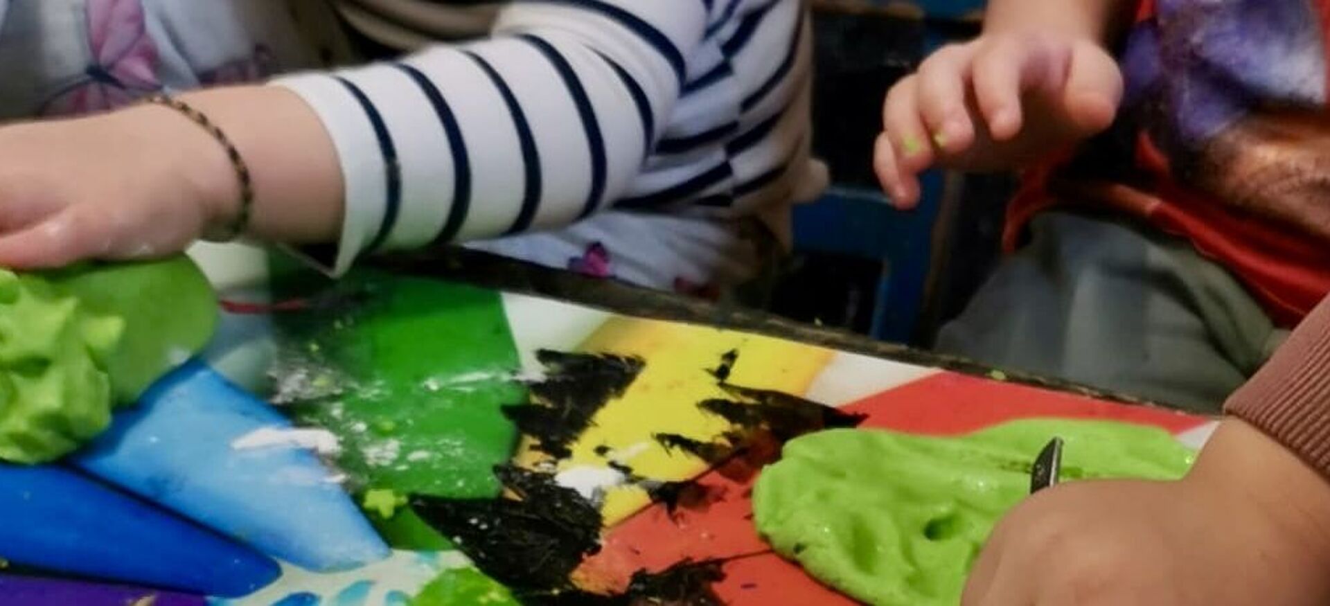 Kinderhände formen grüne Knetmasse auf einem bunt bemalten Tisch mit Regenbogenfarben