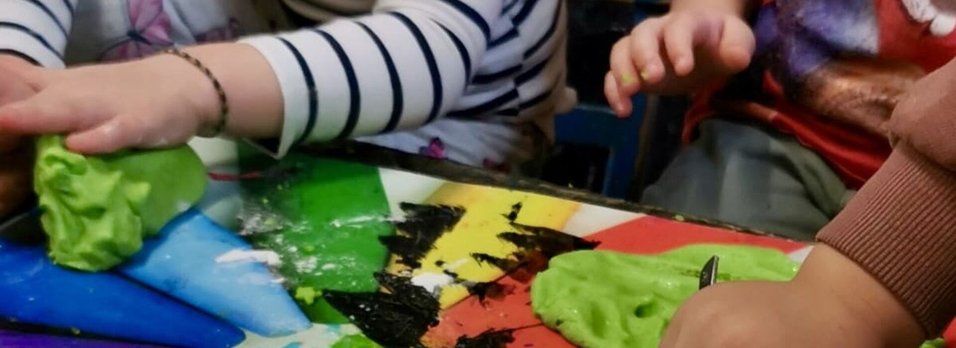 Kinderhände formen grüne Knetmasse auf einem bunt bemalten Tisch mit Regenbogenfarben