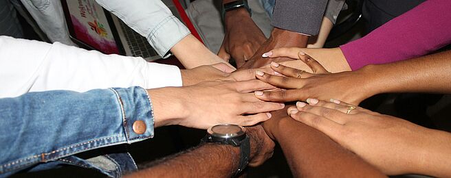 Foto von Rineshkumar Ghirao auf Unsplash Mehrere Hände liegen übereinander in der Mitte eines Kreises