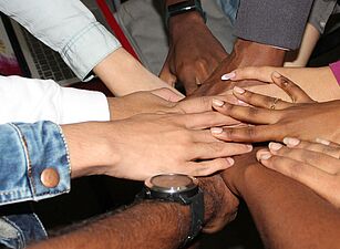 Mehrere Hände liegen übereinander in der Mitte eines Kreises