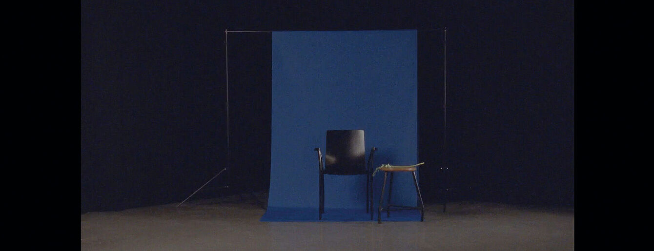 Schwarzer Stuhl vor dunkelblauer Leinwand im dunklem Raum.