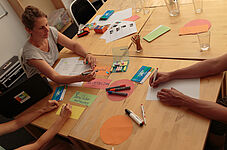 Gruppenberatung mit Trainerin und Arbeitsmaterialien am Tisch