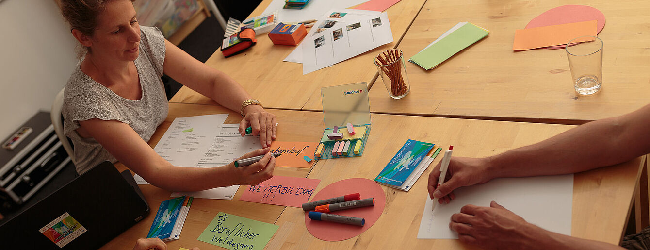 Gruppenberatung mit Trainerin und Arbeitsmaterialien am Tisch