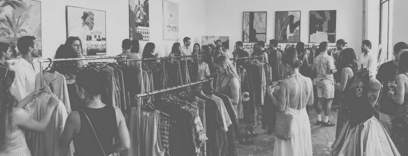 own your closet Menschen in einem hellen Raum mit hohen Fenstern betrachten Kleidung an Kleiderständern und hängen Kleidungsstücke auf