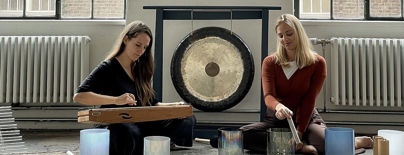 zwei junge Frauen sitzen auf dem Boden vor einer Reihe von Klanginstrumenten