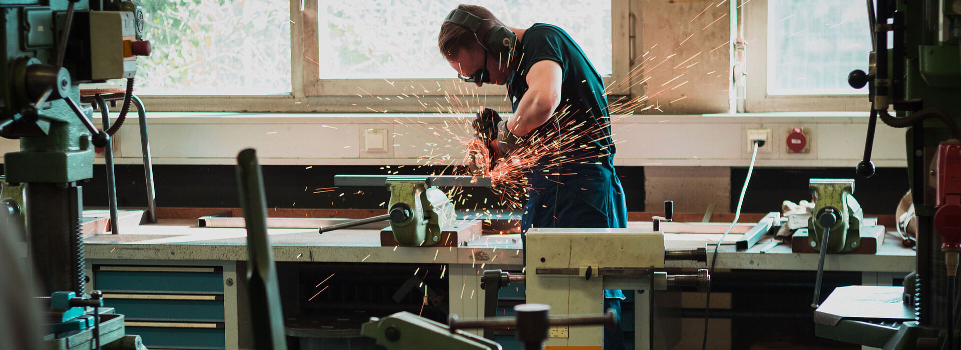 Ein junger Mann arbeitet in einer Werkstatt mit einer Schleifmaschine