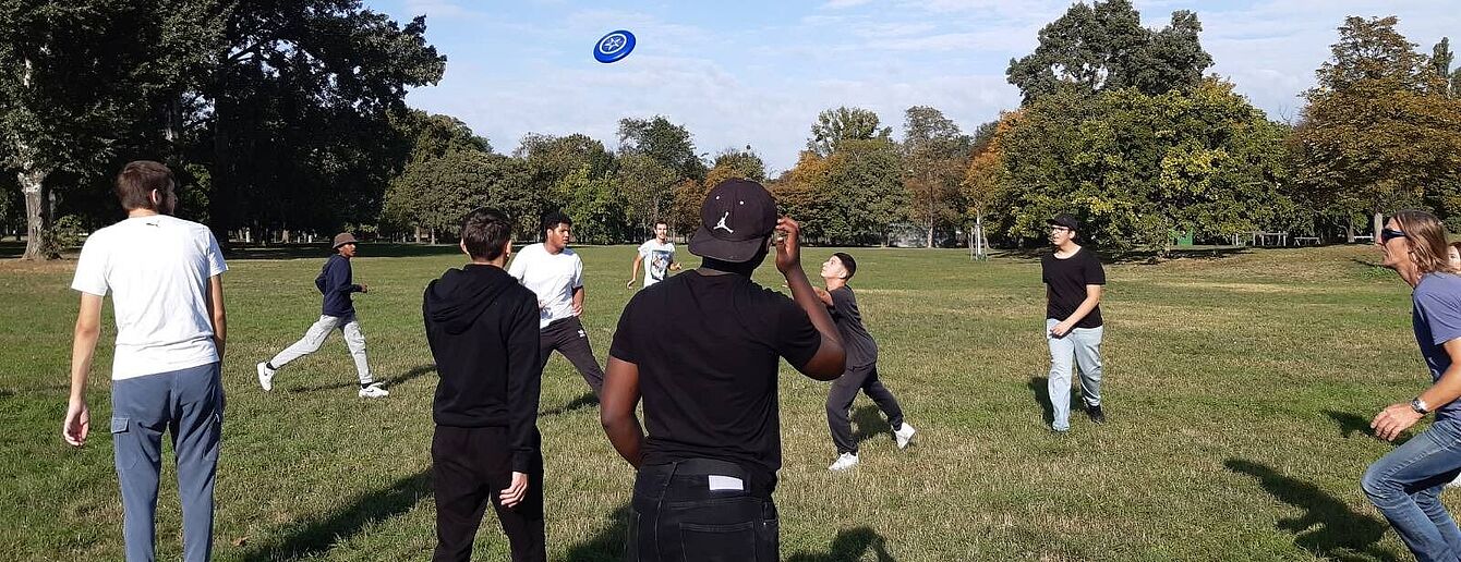 Eine Gruppe Jugendlicher spielt in einer Wiese Frisbee