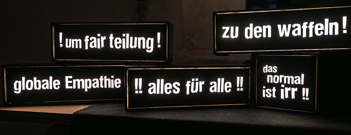 schwarzer Hintergrund, darauf verteilt Schilder mit Sprüchen wie "Zu den Waffeln!" oder "globale Empathie"