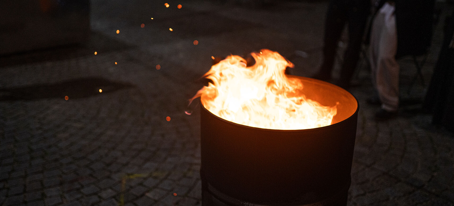 Das Bild zeigt eine Metalltonne mit brennendem Feuer