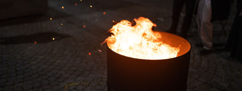 Das Bild zeigt eine Metalltonne mit brennendem Feuer