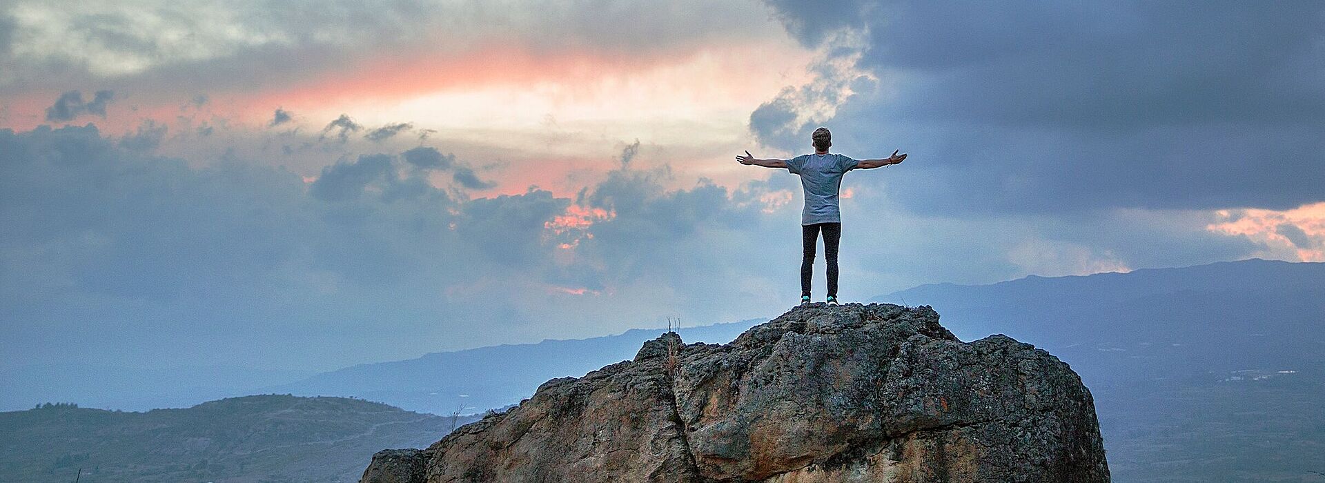 Ein Mann steht mit ausgestreckten Händen auf einer Bergsptze