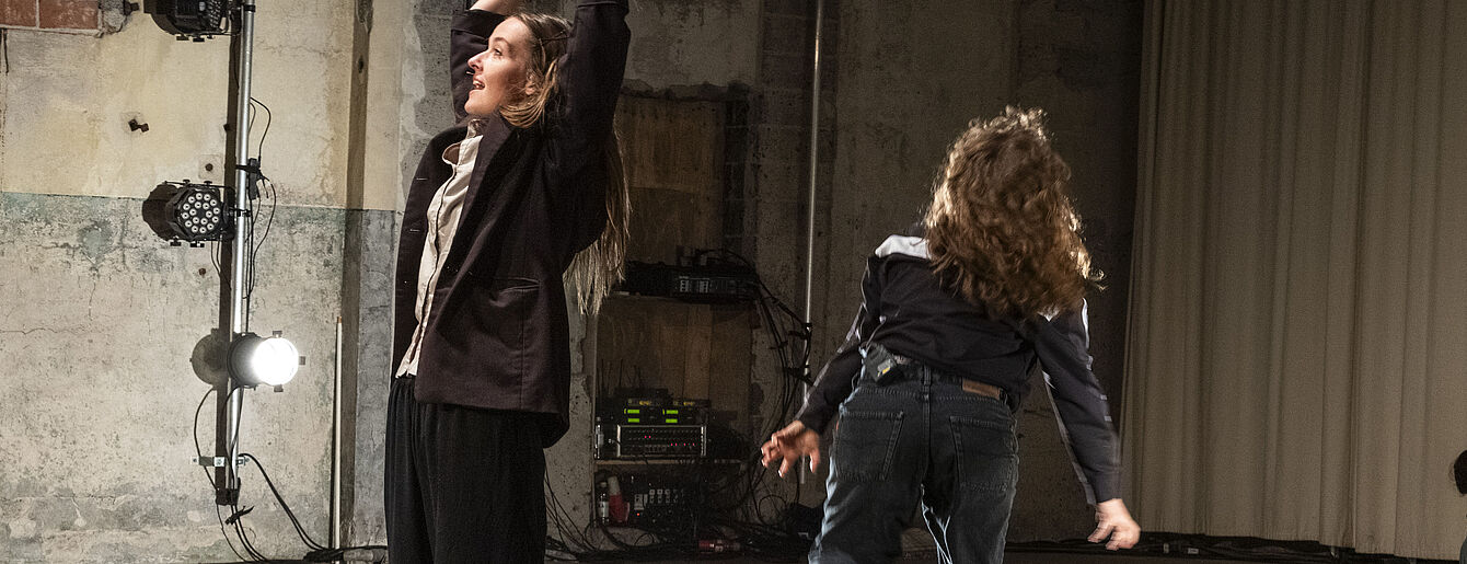 Zwei Personen tanzen in einem Raum mit Betonwänden und Bühnenbeleuchtung während des Workshops 'Choreo Constellating'