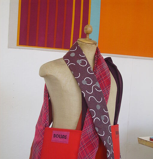 Schaufensterpuppe mit roter Tasche und gemustertem Schal vor farbigen Wandbildern