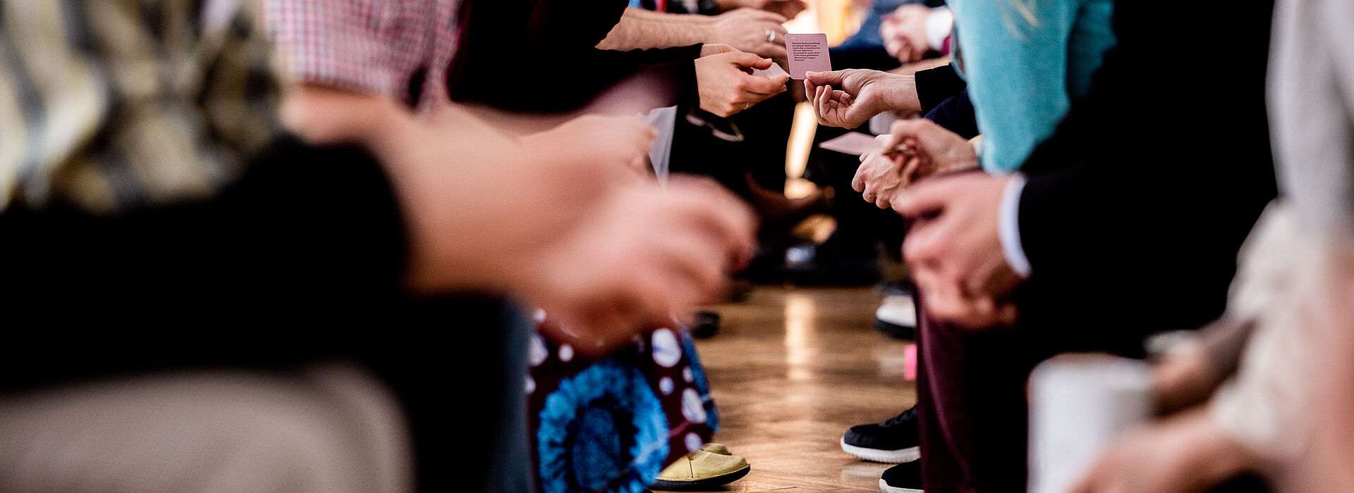 Menschen sitzen sich in zwei Reihen gegenüber und tauschen kleine Karten aus, Fokus auf Hände und Karten